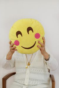 Photo d'une résidente tenant un coussin en forme d'émoji qui sourit devant son visage