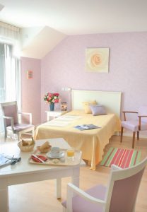 Appartement meublé, un lit simple, une tapisserie mauve et un plateau de petit-déjeuner sur la table